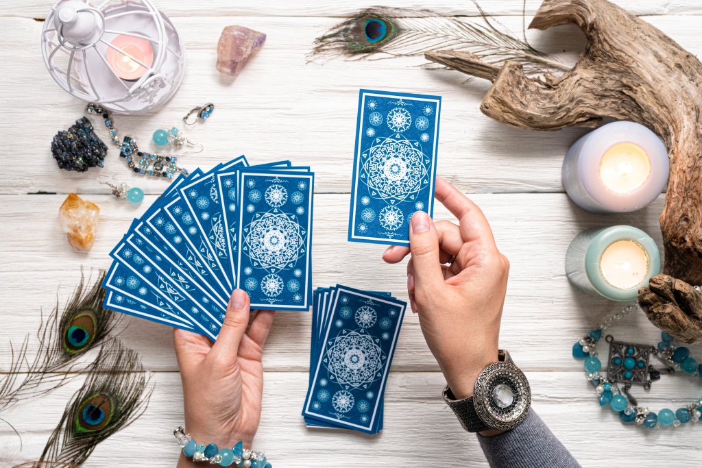 Fortune teller woman's hands holding blue tarot cards over a white wooden table background.
